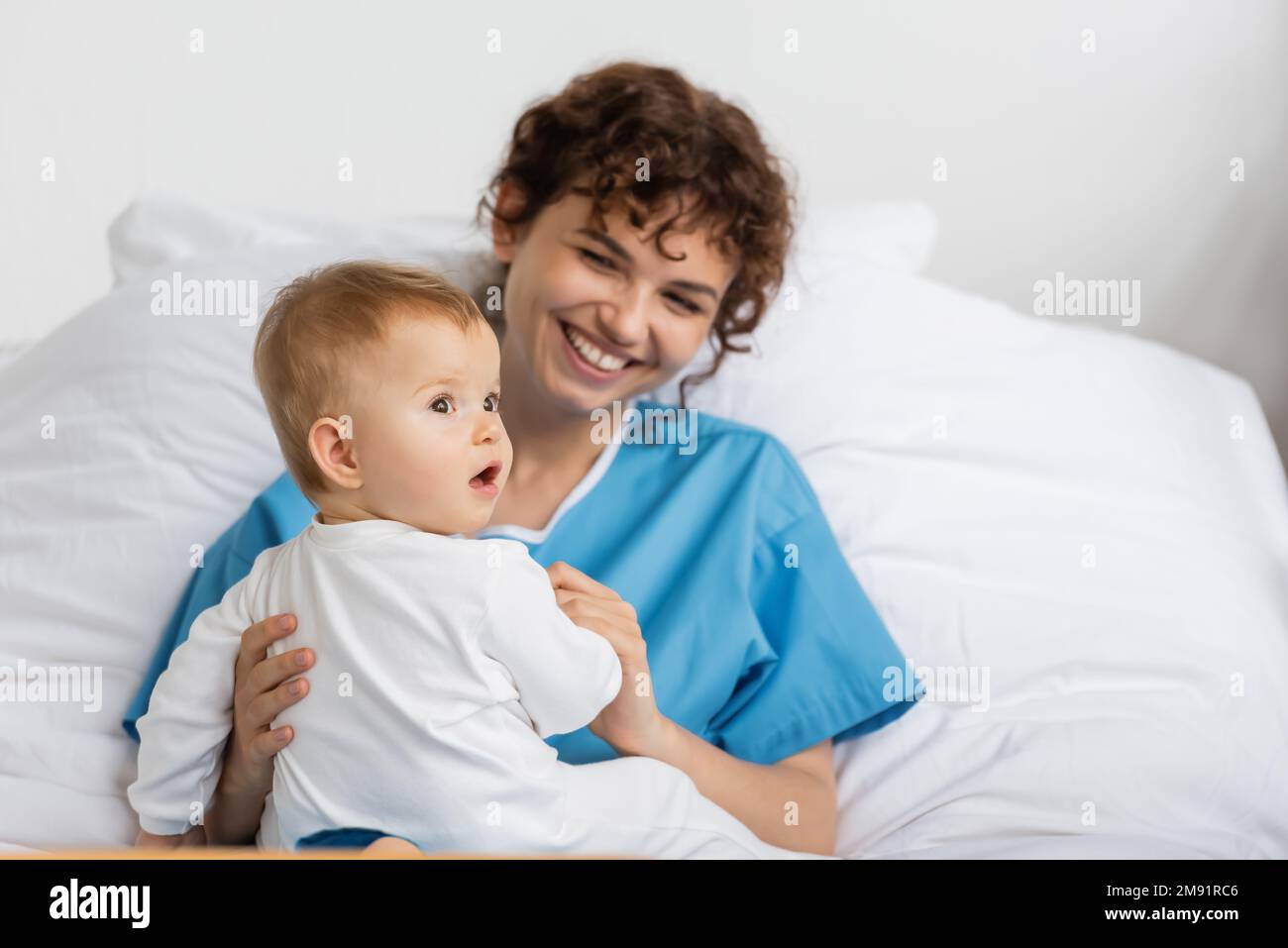 little baby with open mouth looking away near smiling mother in hospital ward,stock image Stock Photo