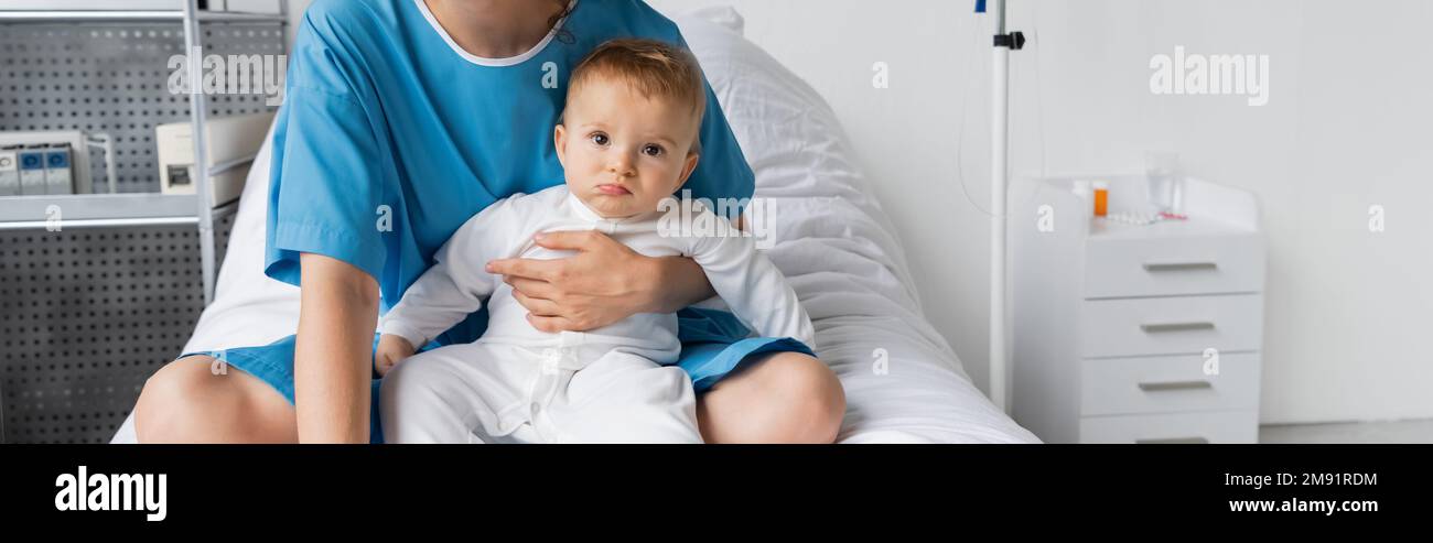 woman in patient gown sitting on hospital bed and holding little daughter in romper, banner,stock image Stock Photo