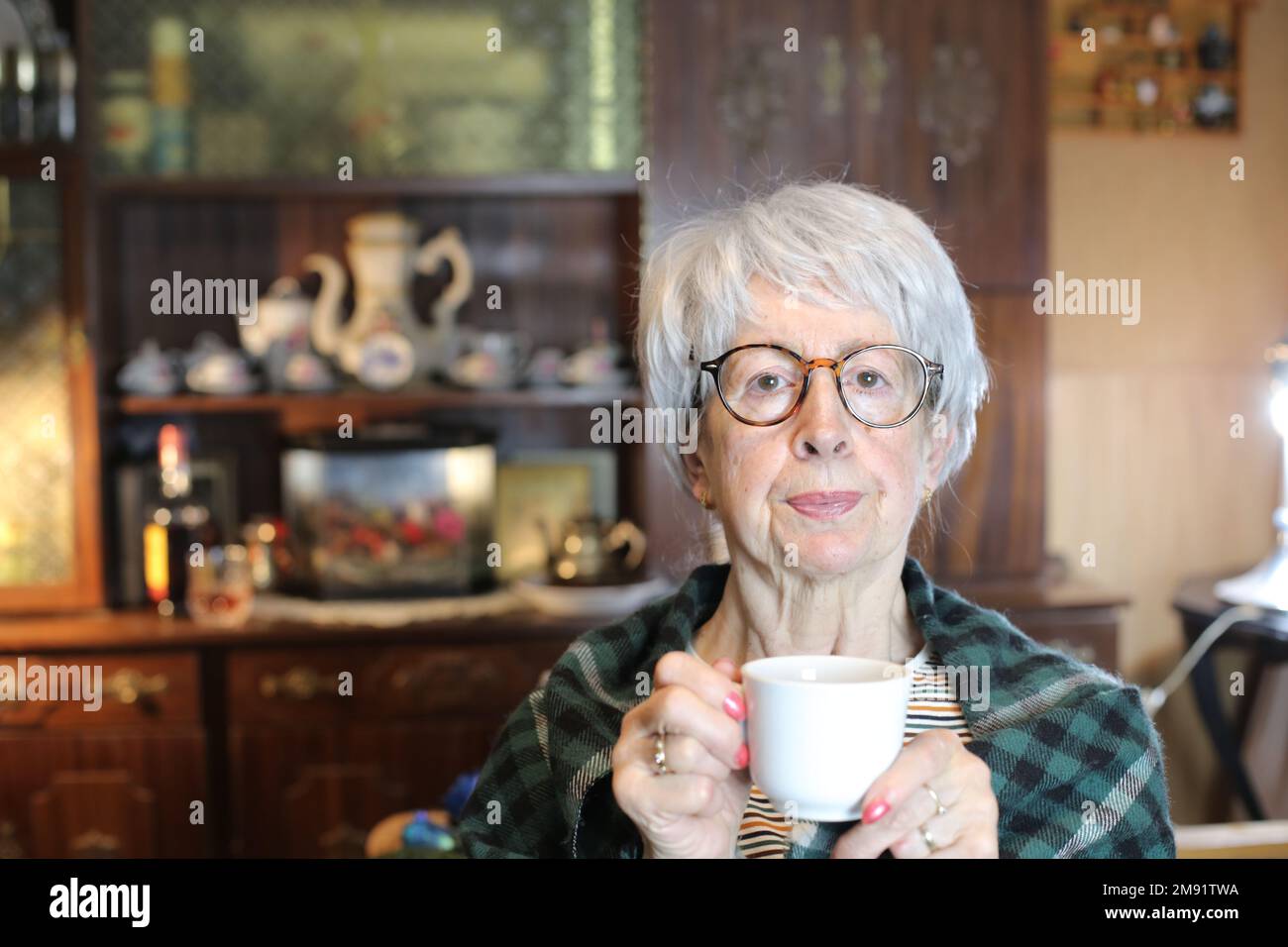 Senior woman covered in a blanket holding warm drink Stock Photo