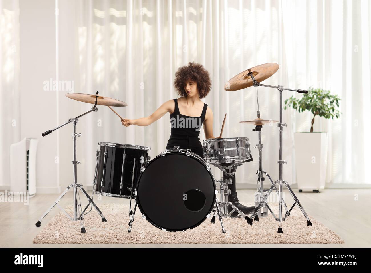 Young female playing drums inside a room Stock Photo