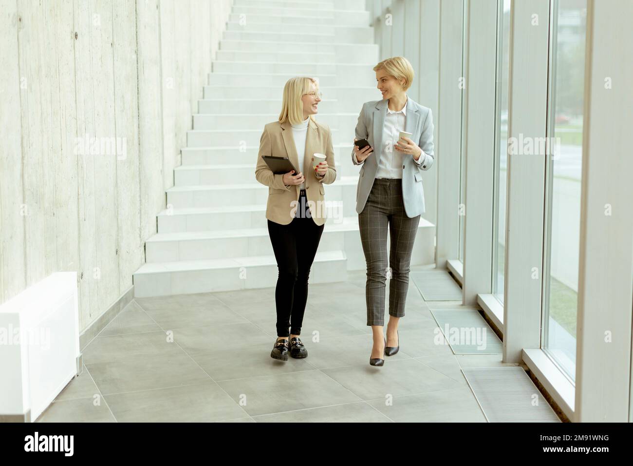 Two business women walking with digital tablet and mobile phone in the office corridor Stock Photo
