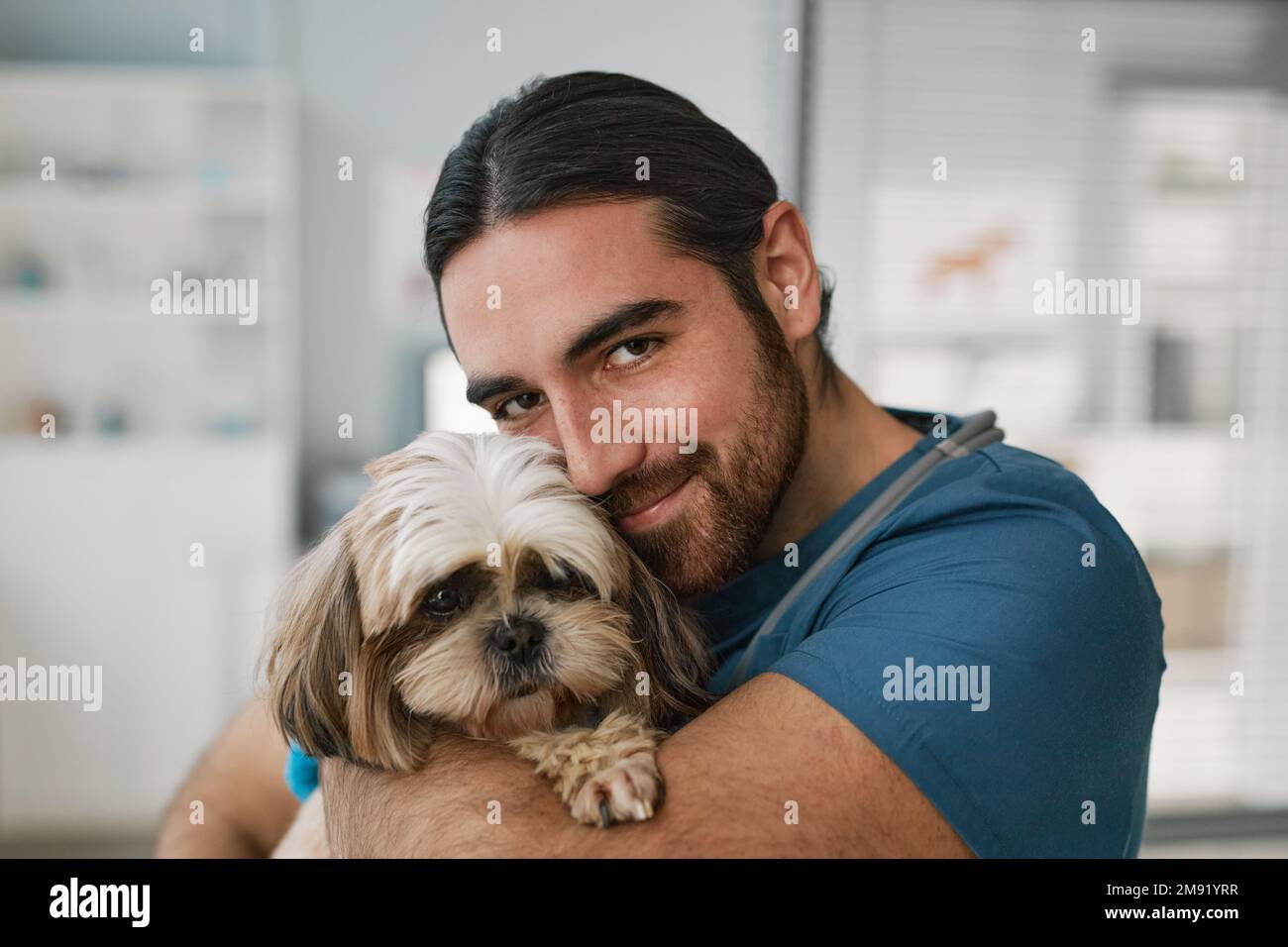 Young smiling vet clinician holding cute fluffy yorkshire terrier and looking at camera while taking care of pet of one of veterinary clients Stock Photo