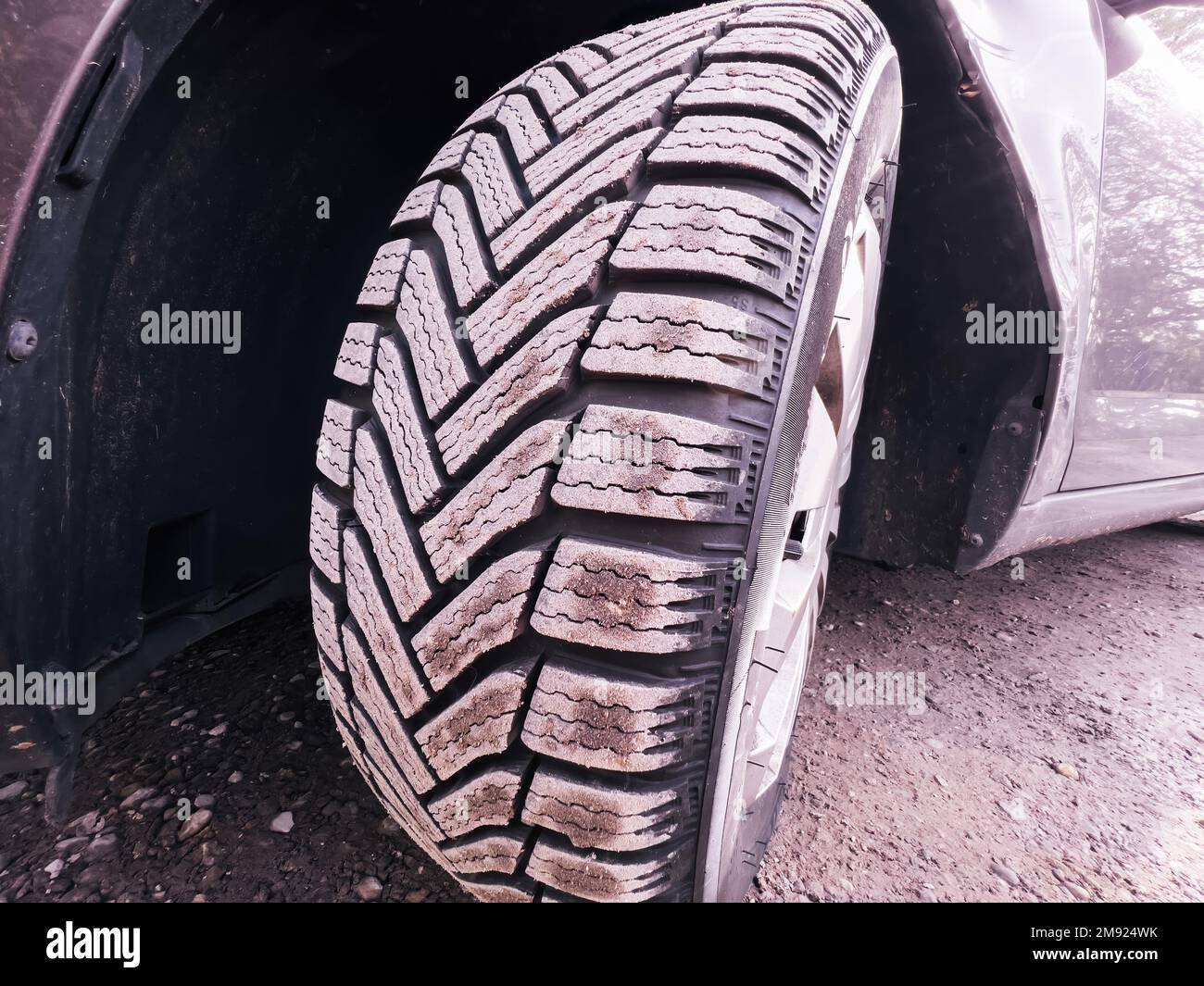 Car front with winter tire covered with dust - brand new wheels for the upcoming cold season - mandatory protection during cold weather - warm color cast Stock Photo