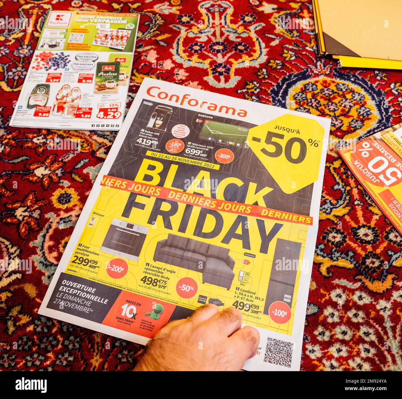 Paris, France - Dec 2, 2022: Advertising leaflets of Conforama supermarket chain selling furniture, electronics home object - man reading on the living room silk rug Stock Photo