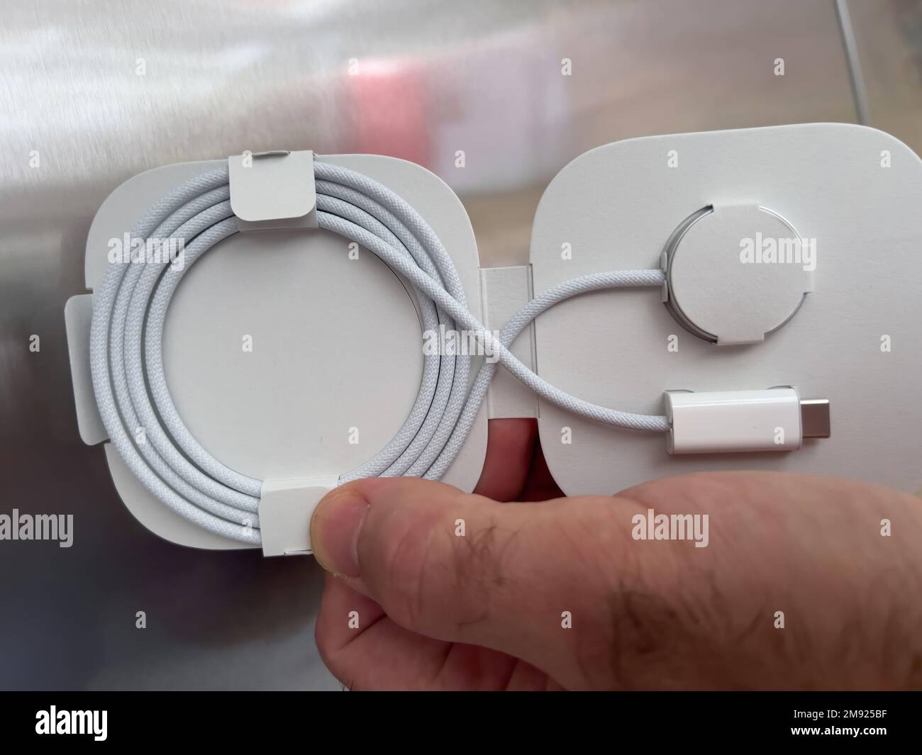 Paris, France - Oct 18, 2022: POV male hand holding against steel background cardboard box of new packaged Apple Watch Magnetic Fast Charger to USB-C cable Stock Photo