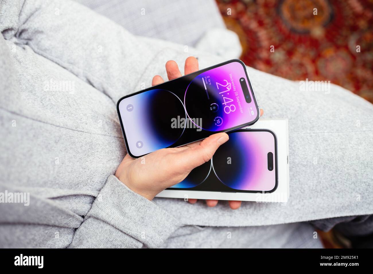 London, United Kingdom - Sep 28, 2022: POV woman hand holding the package showing new Deep Purple Apple iPhone 14 Pro Max the sixteenth-generation flagship iPhones with no SIM cards and Dynamic Island feature always on display Stock Photo