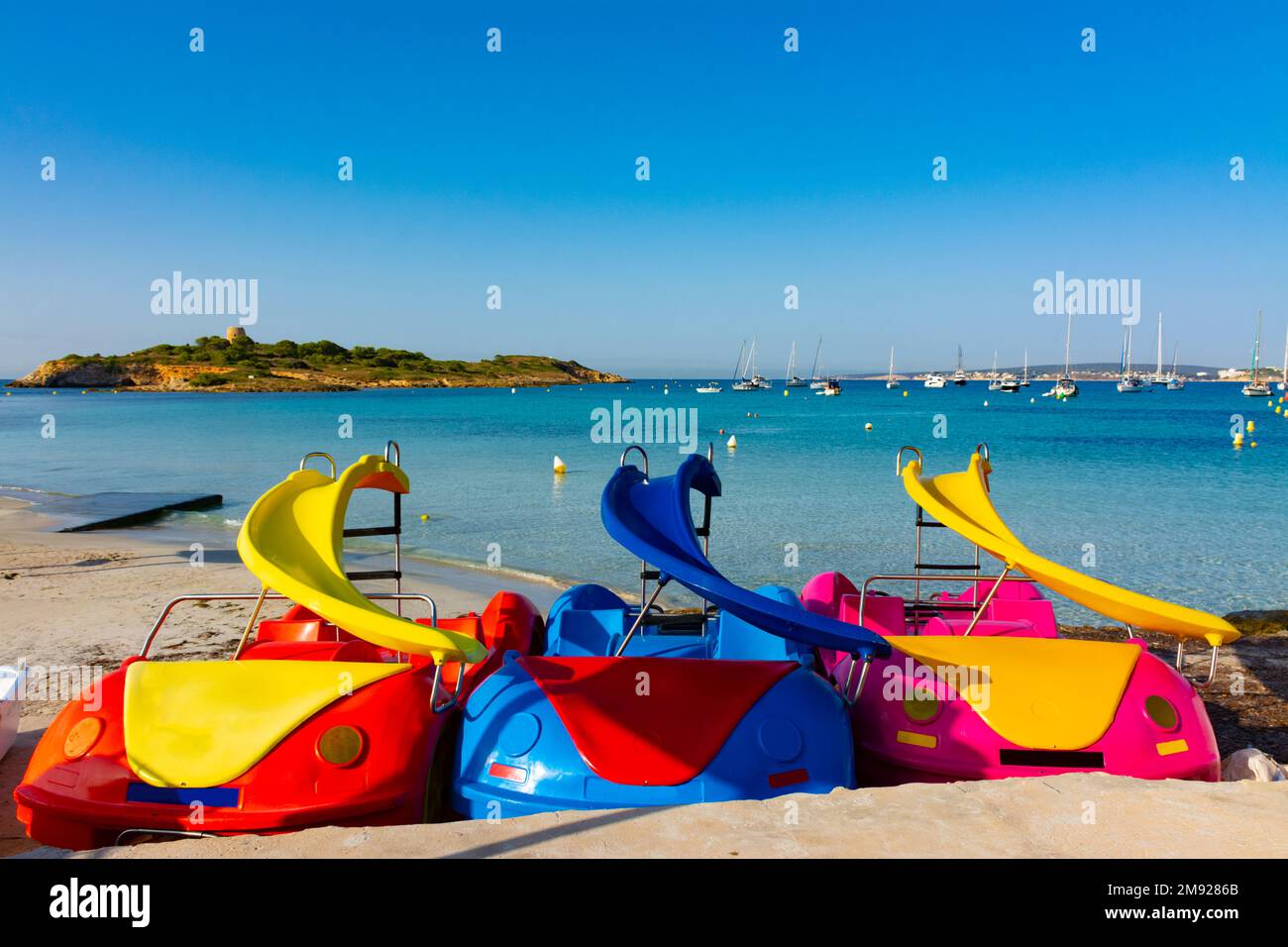 Some pedal boats on the sand in the Xinxell cove, in Ses Illetes, Majorca, Spain. Moored boats an Palmanova at background Stock Photo