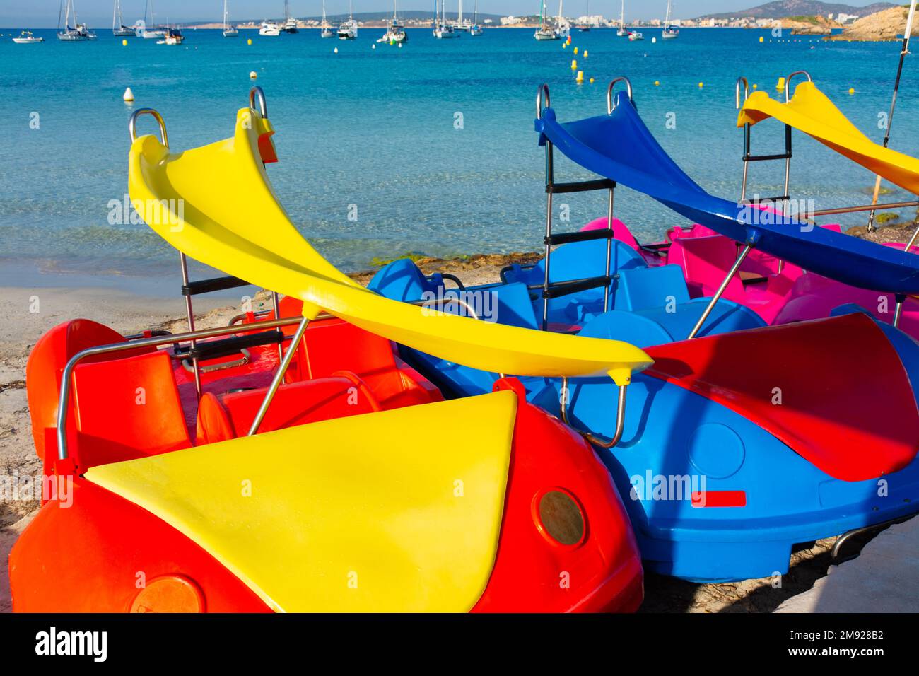 Colorful pedal boats on the sand in the Xinxell cove, moored sailboats and Palmanova at background, in Majorca, Balearic islands, Spain Stock Photo