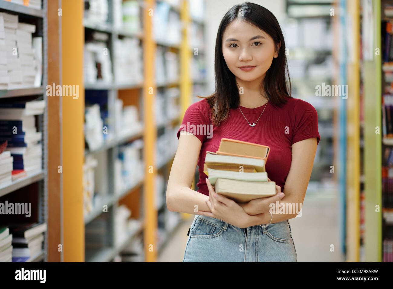 Portrait of smiling teenage girl with stack of books standing in ...