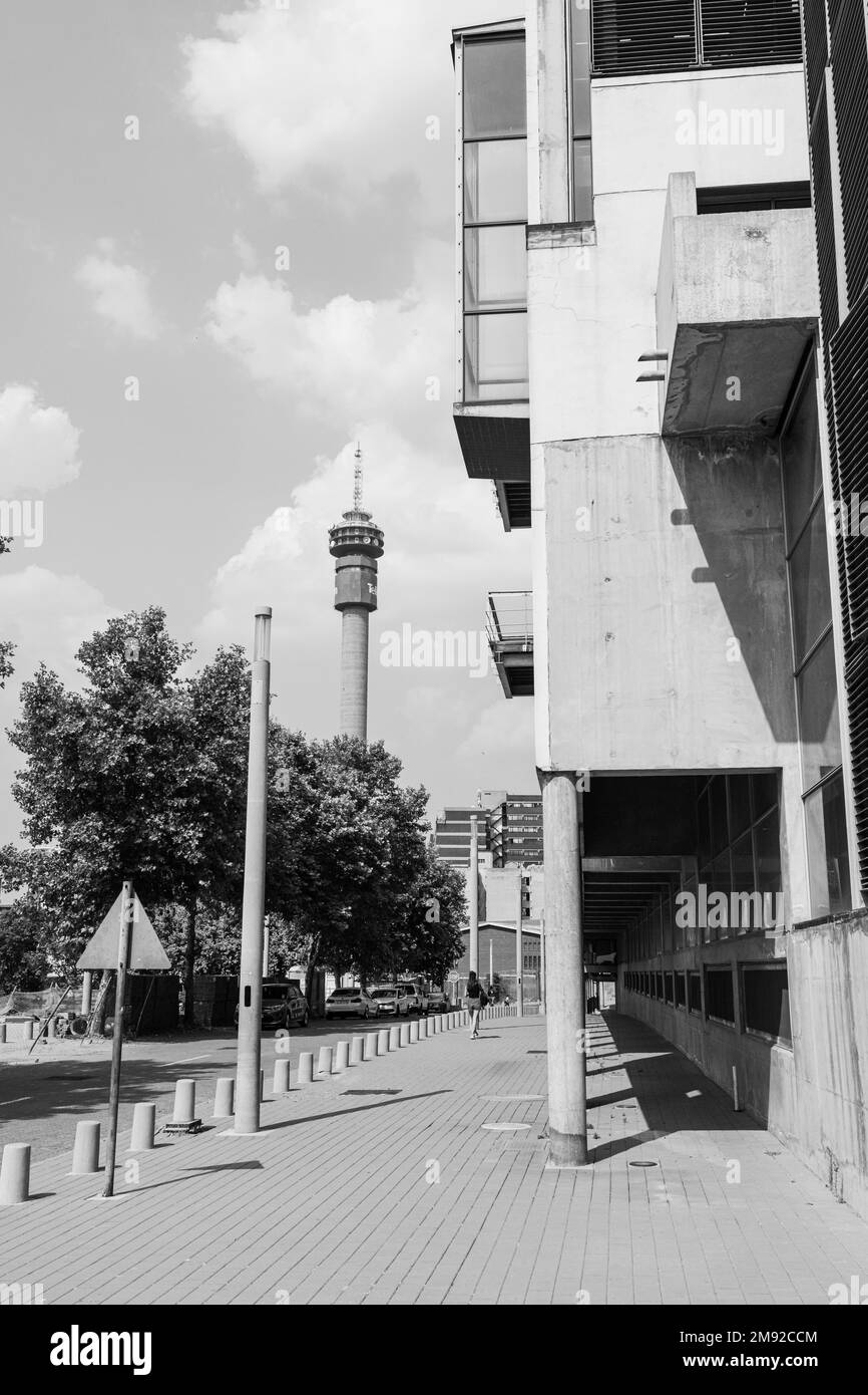 A vertical grayscale shot of a sidewalk with apartment buildings and signboards near the trees in Johannesburg, South Africa Stock Photo