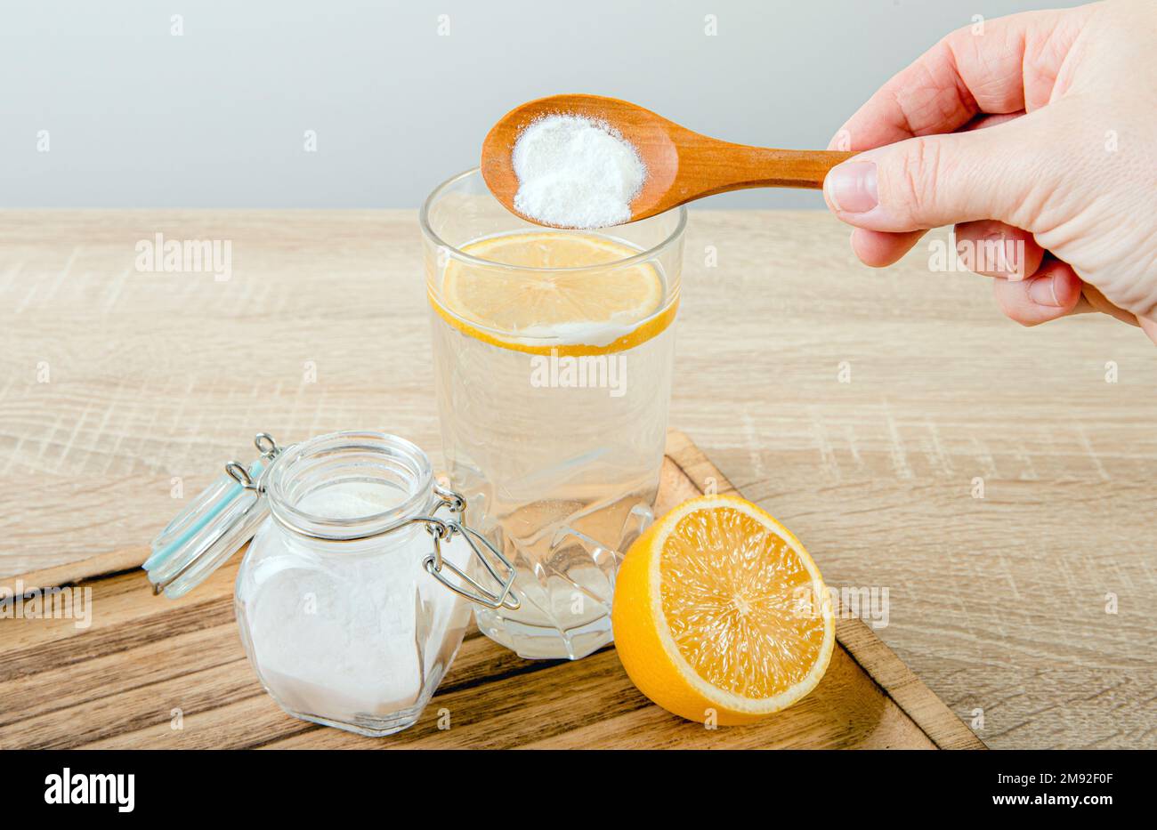 Close up of woman hand pouring baking soda in drinking glass with water and lemon juice, health benefits for digestive system concept. Stock Photo