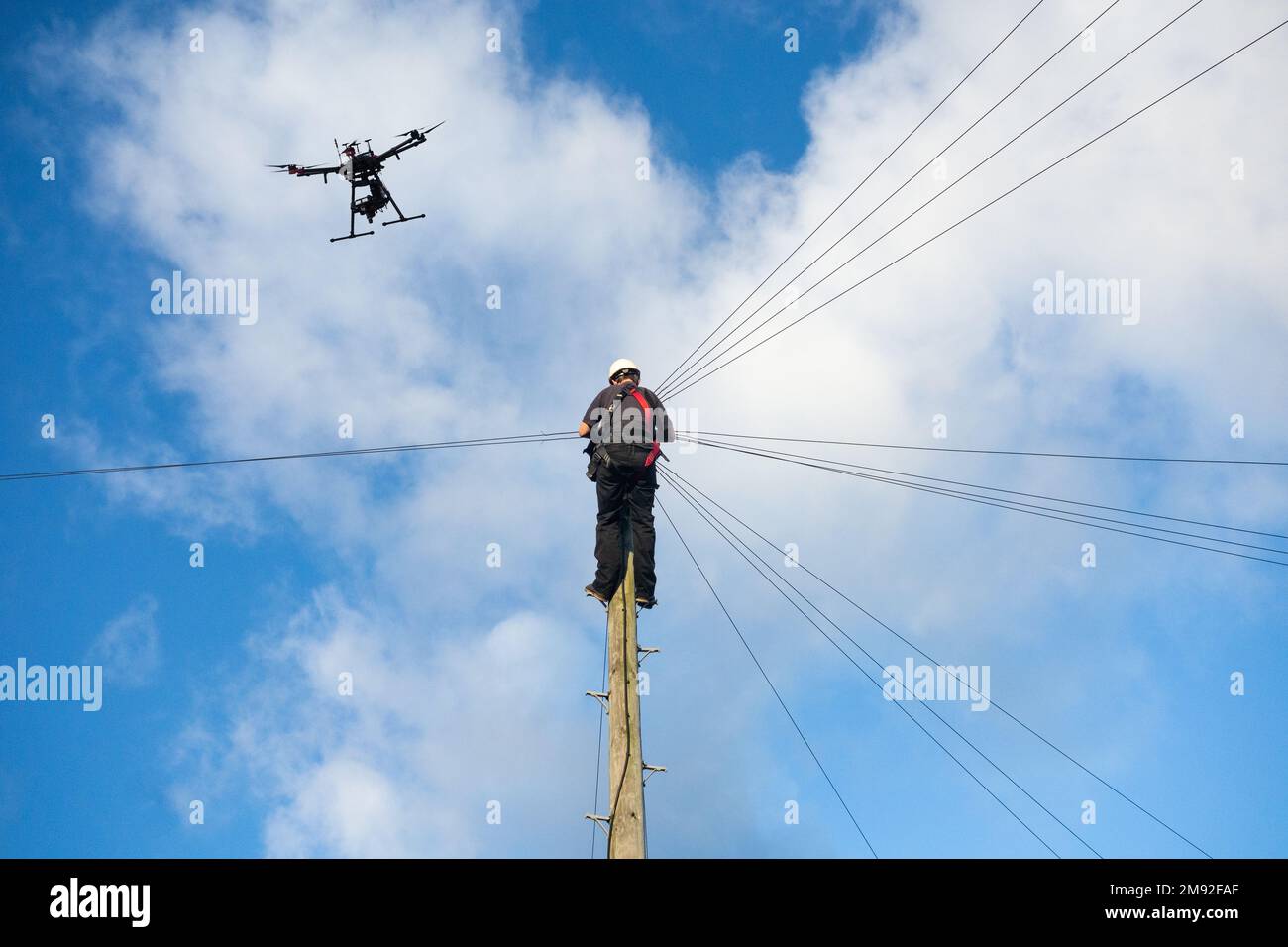 Telecommunications,Telecom engineer working up telegraph pole with drone flying above. Drone technology, Broadband, 5g, internet...concept. UK Stock Photo