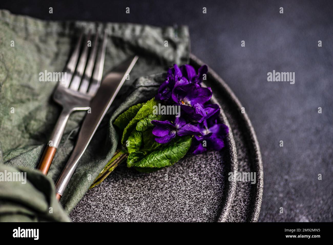 Spring table setting with wild blue viola flower on black plate set Stock Photo