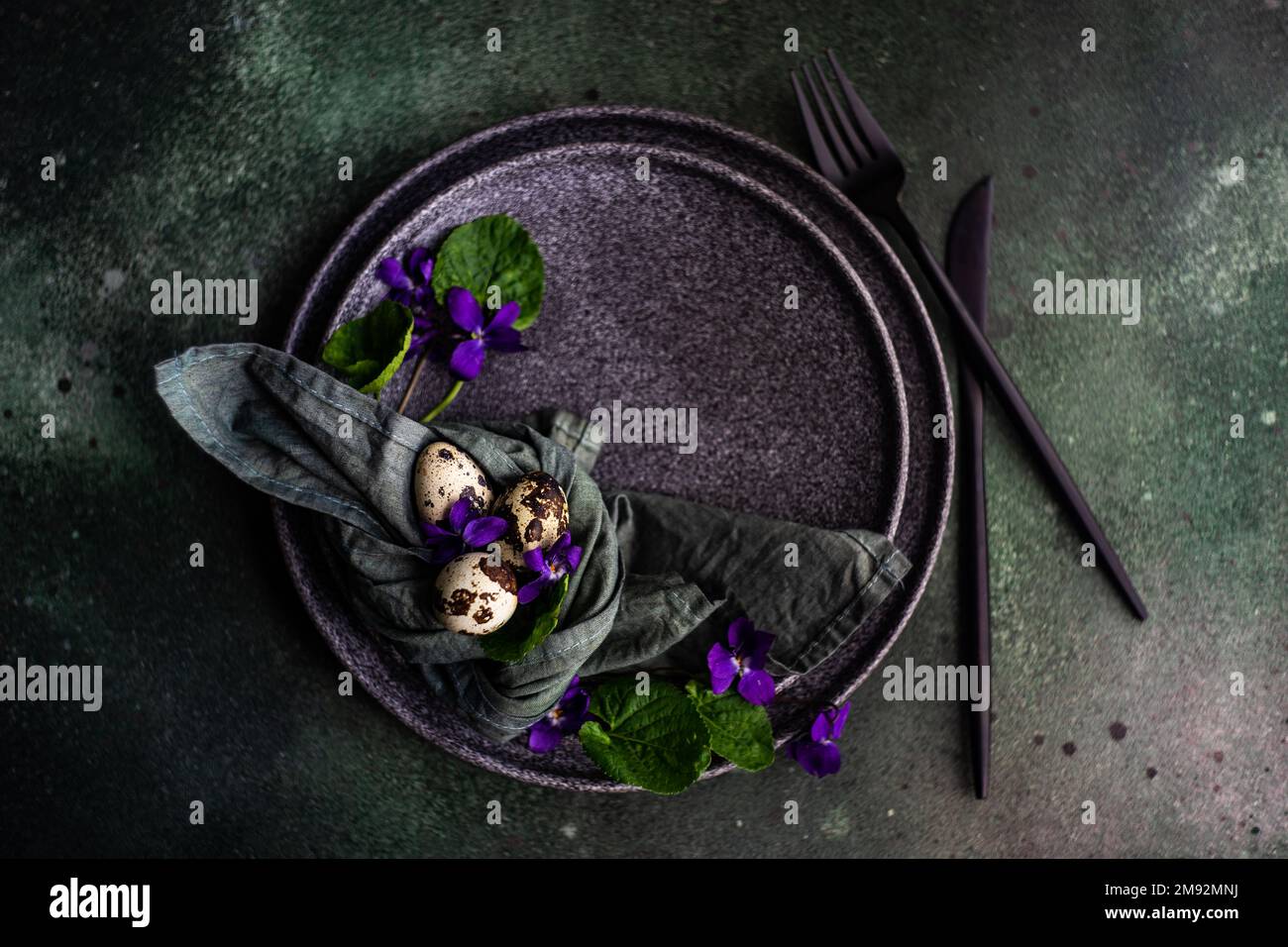 Spring table setting with wild blue viola flower on black plate set Stock Photo