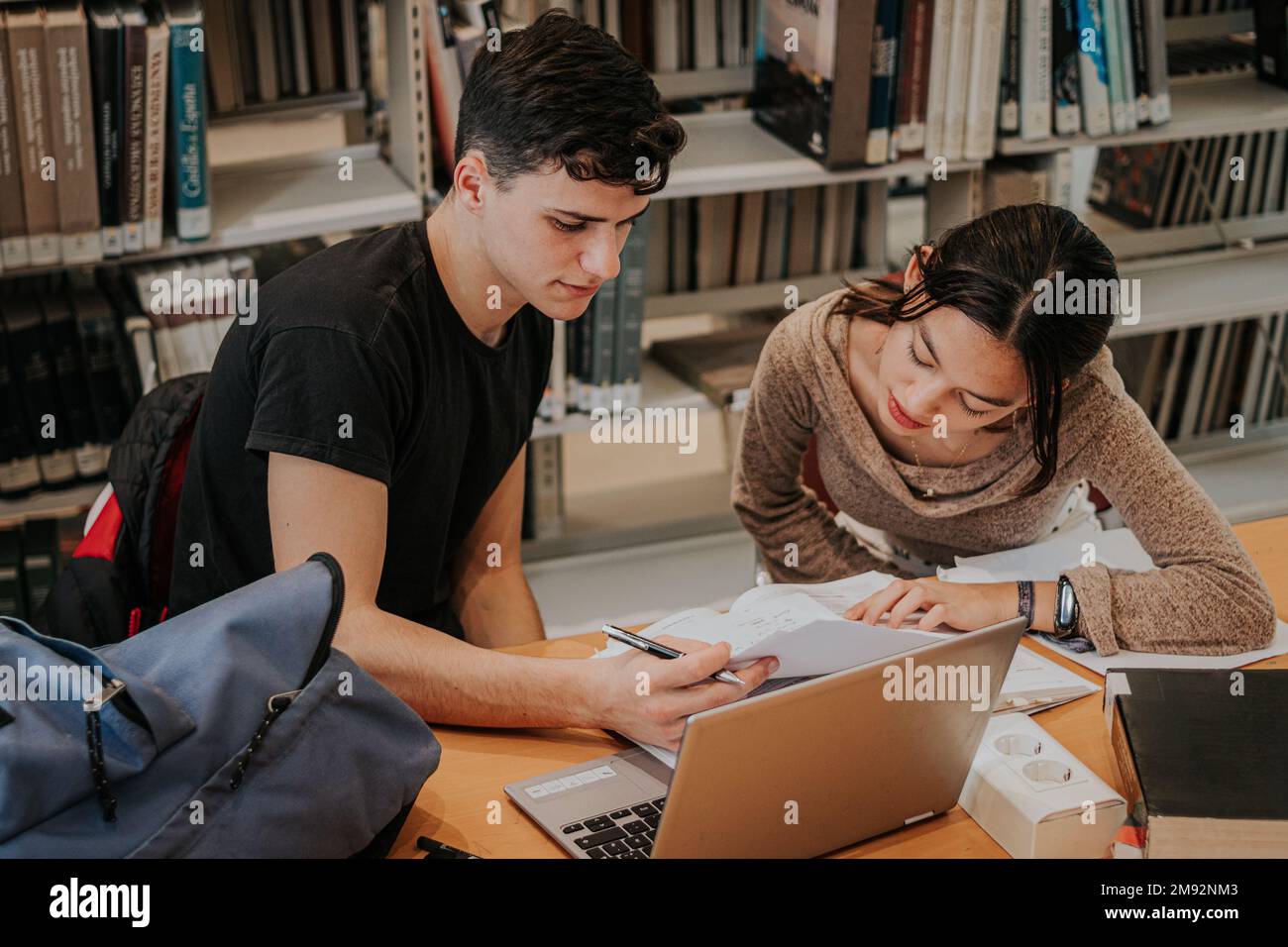 Concentrated teen students in casual outfits sitting at wooden table with laptop and working on university project together while studying in library Stock Photo