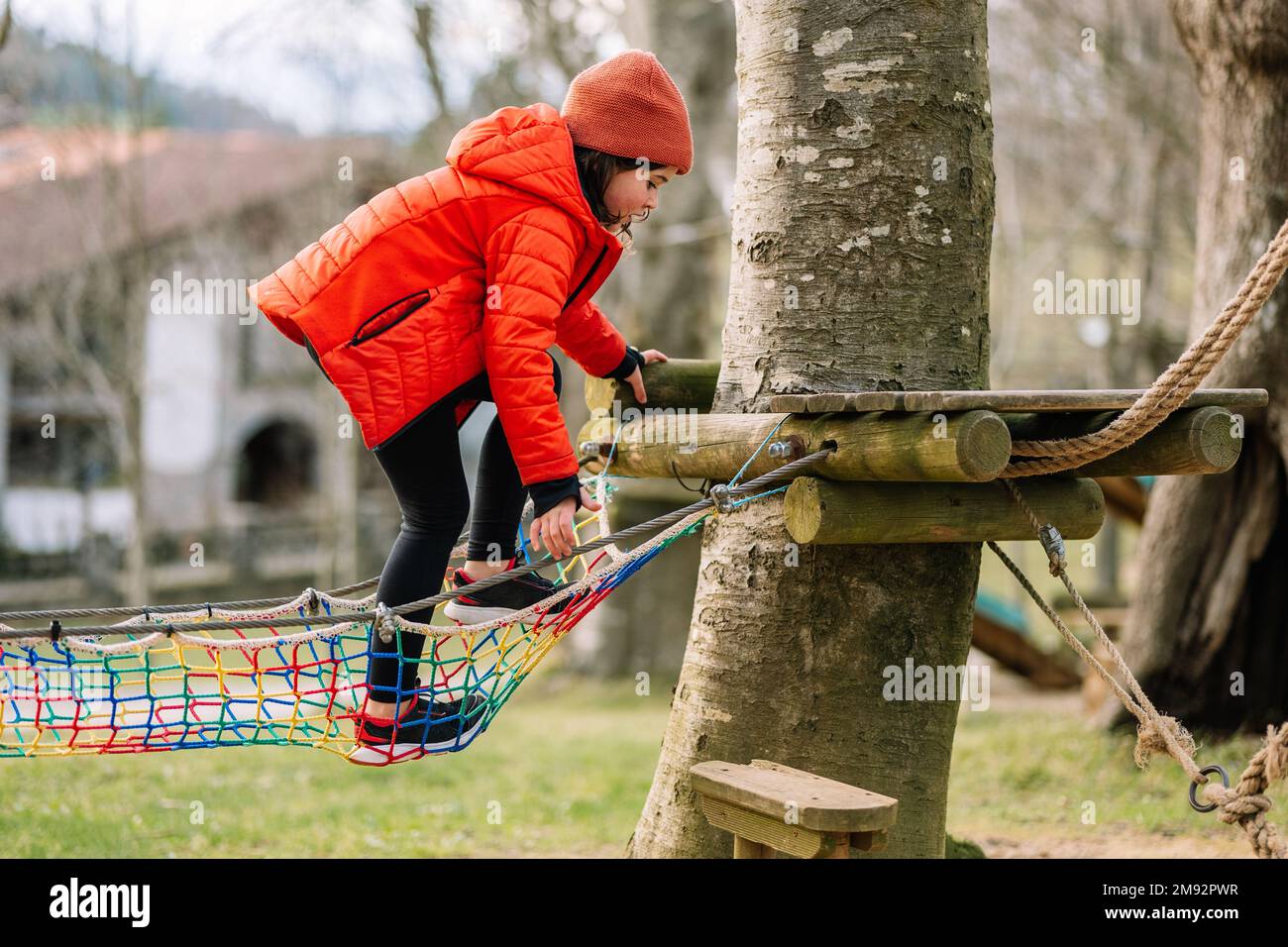 Side view full body of focused kid in warm clothes hanging on rope while walking on net in autumn park during weekend Stock Photo