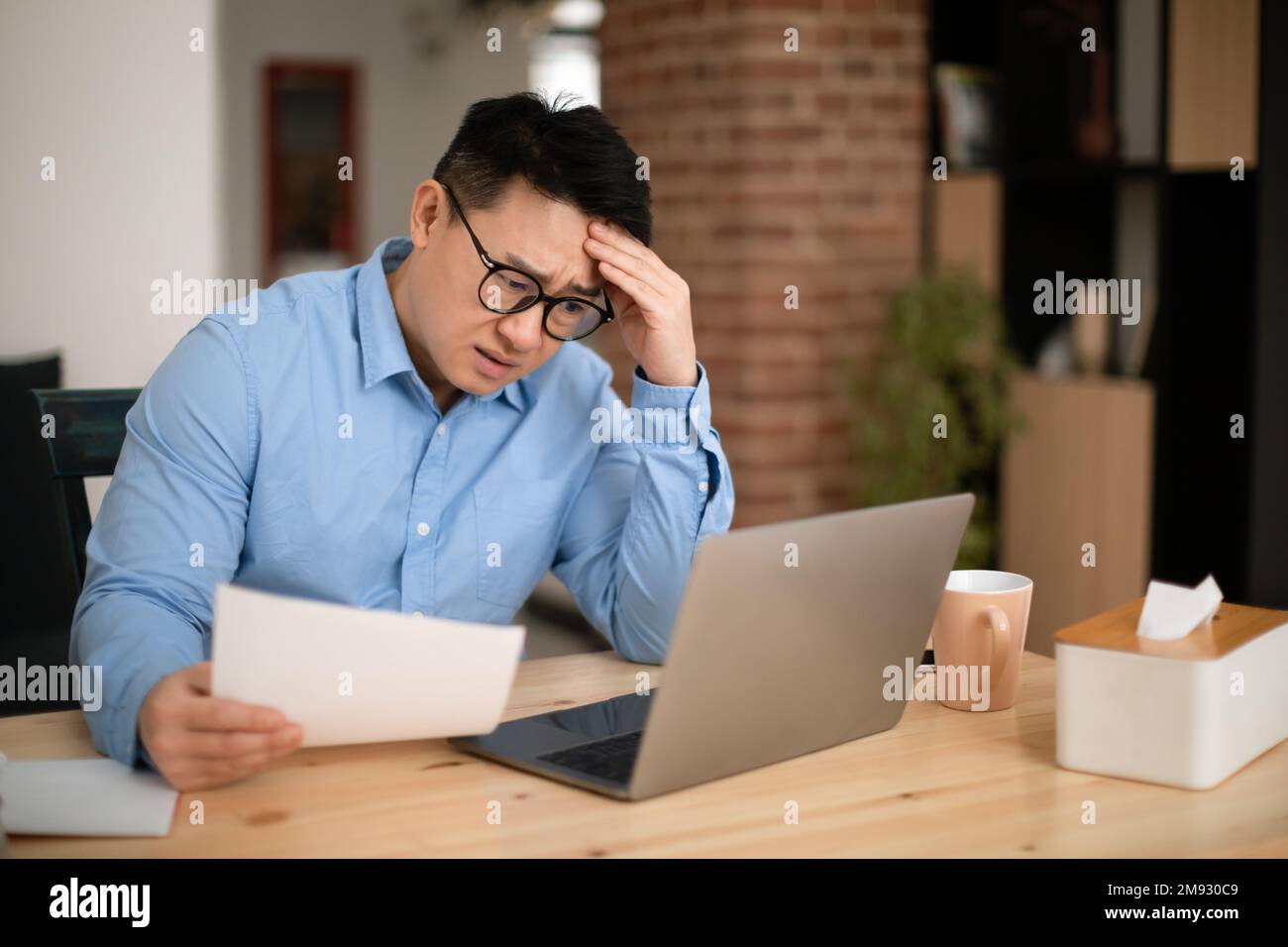 Stressed middle aged asian businessman holding papers, reading bills or tax form, having financial problem Stock Photo