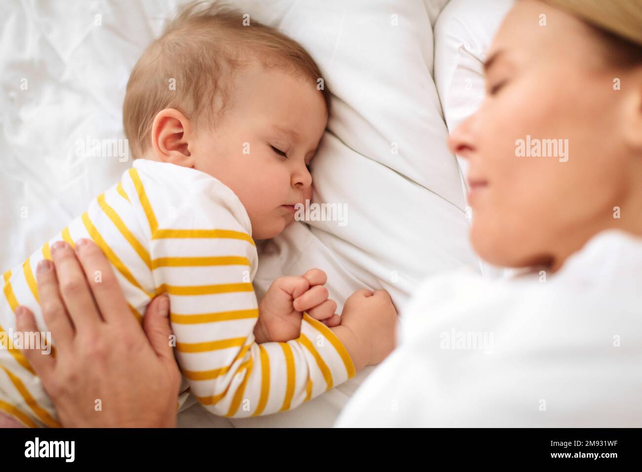 Loving caucasian mother hugging sleeping baby, lying in bed, high angle shot, focus on kid Stock Photo