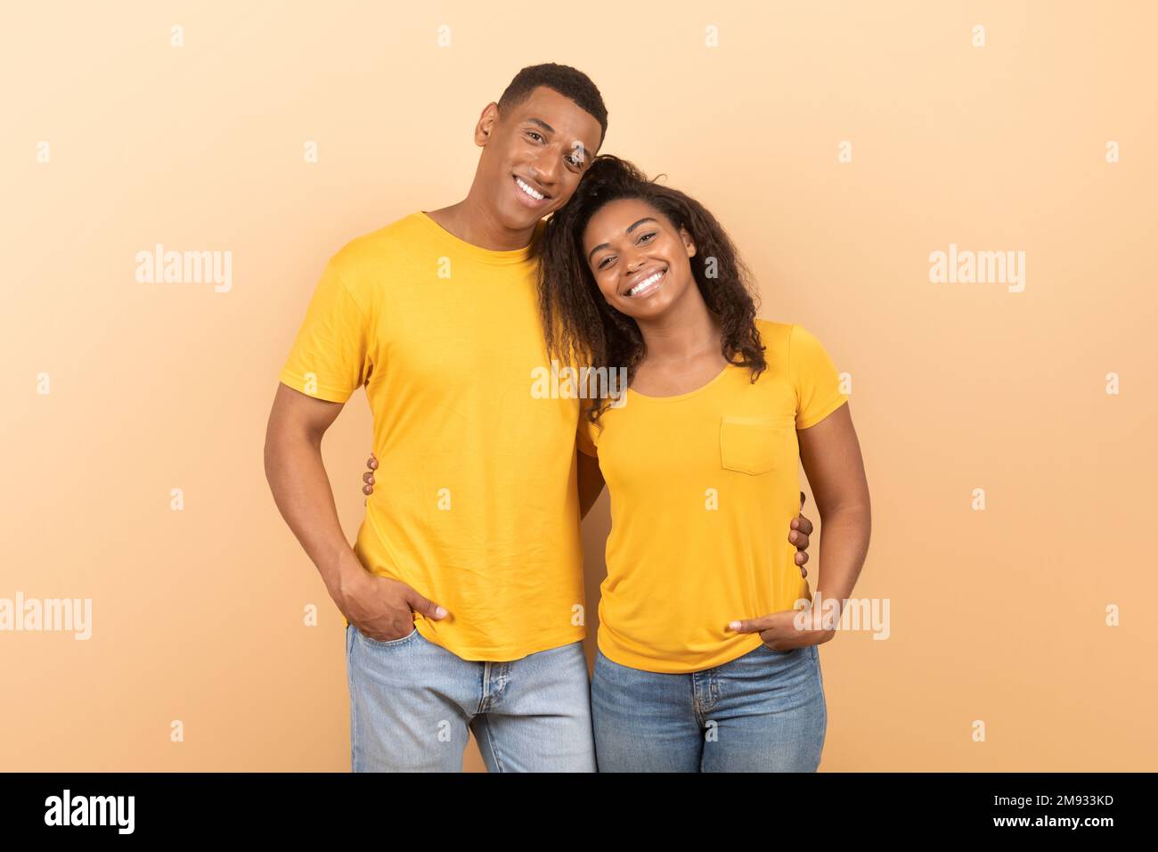 Portrait of loving young black spouses hugging and smiling at camera over yellow studio background Stock Photo