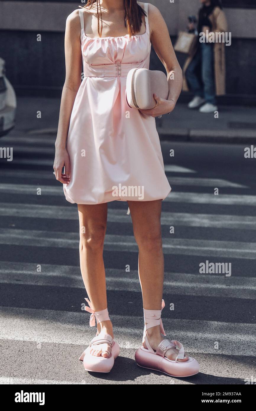 Milan, Italy - February 25, 2022: Crop female in stylish pink dress and sandals with purse standing on sunlit in Milan, Italy. Stock Photo