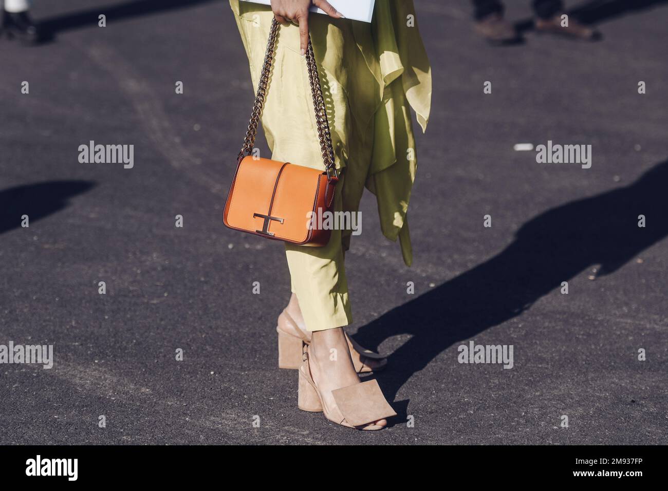 Milan, Italy - February 26, 2022: Female in stylish bright yellow asymmetrical pants with orange bag and beige sandals. Stock Photo