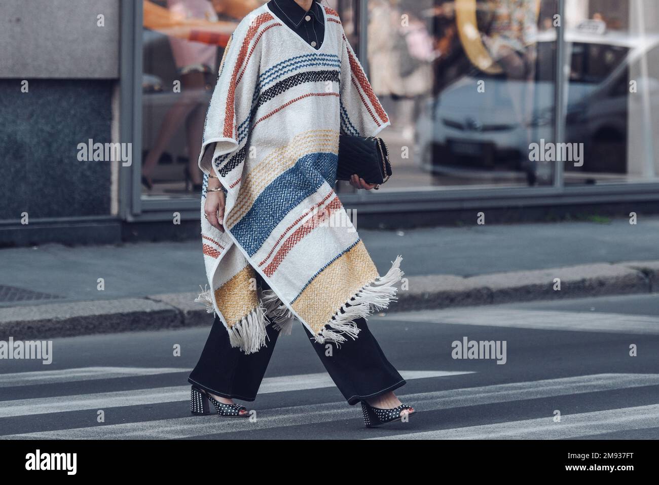 Milan, Italy - February 26, 2022: Woman in stylish poncho walking on the street in daytime. Stock Photo