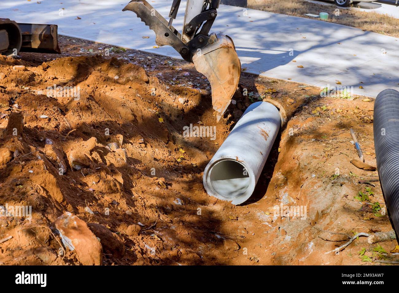 Worker working with tractor lift to install sewage pipes in ground is