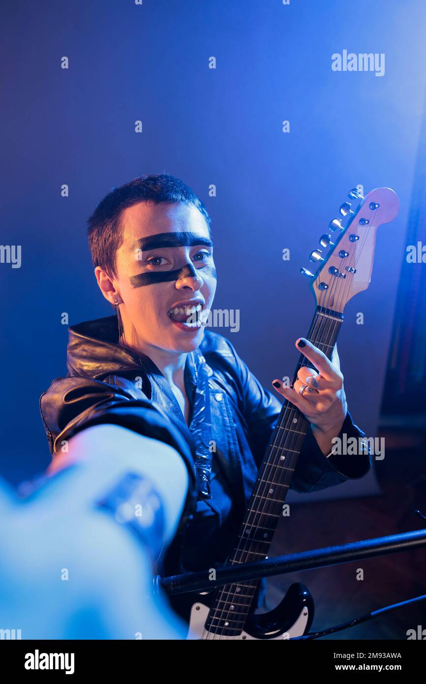 Punk rocker showing rock sign on camera and playing guitar, creating