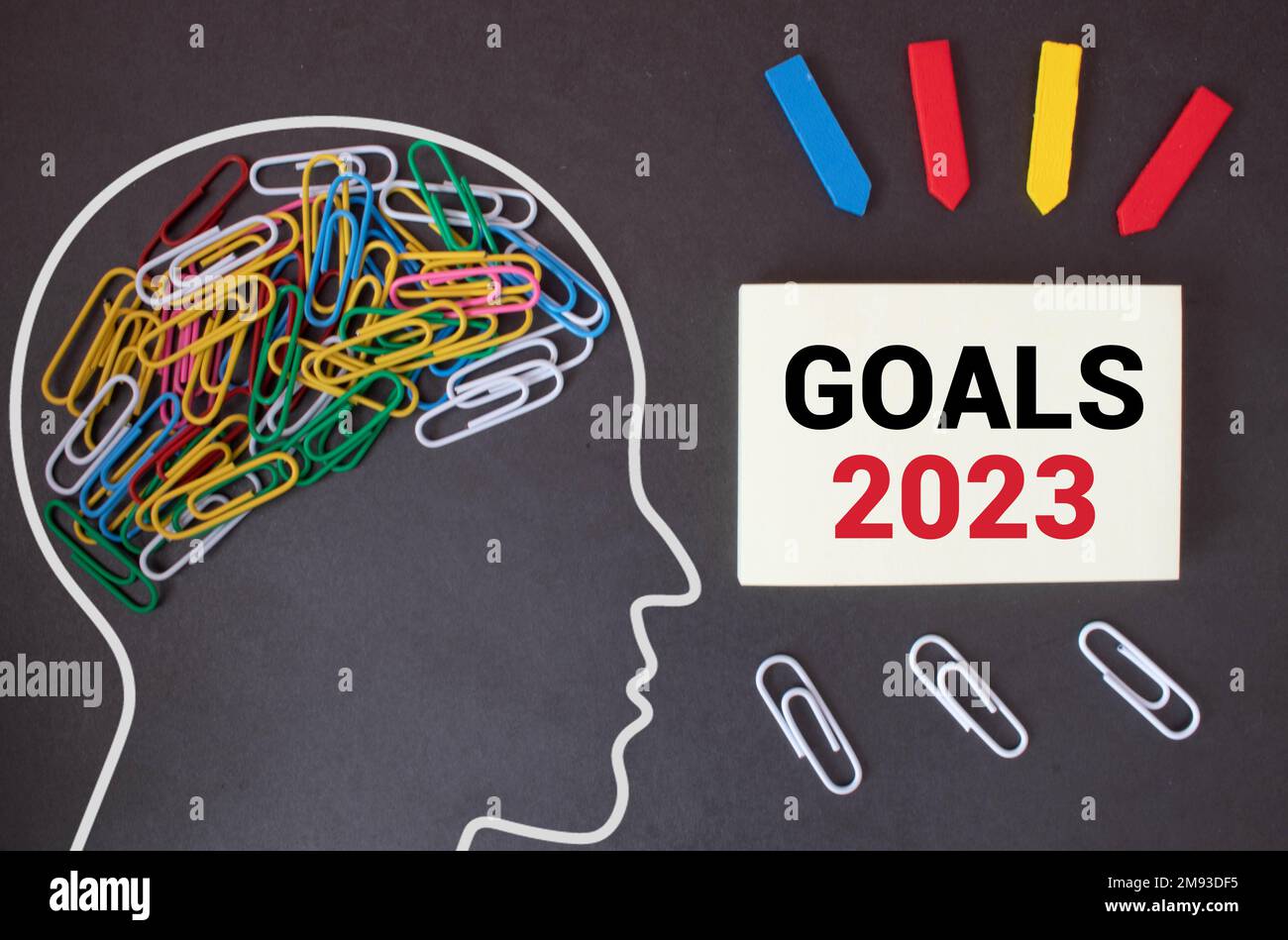 2023 goals message on pink note paper with alarm clock and pen