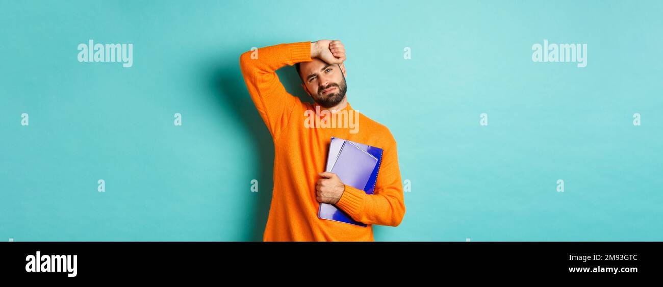 Education. Tired male student holding notebooks and wiping sweat off ...