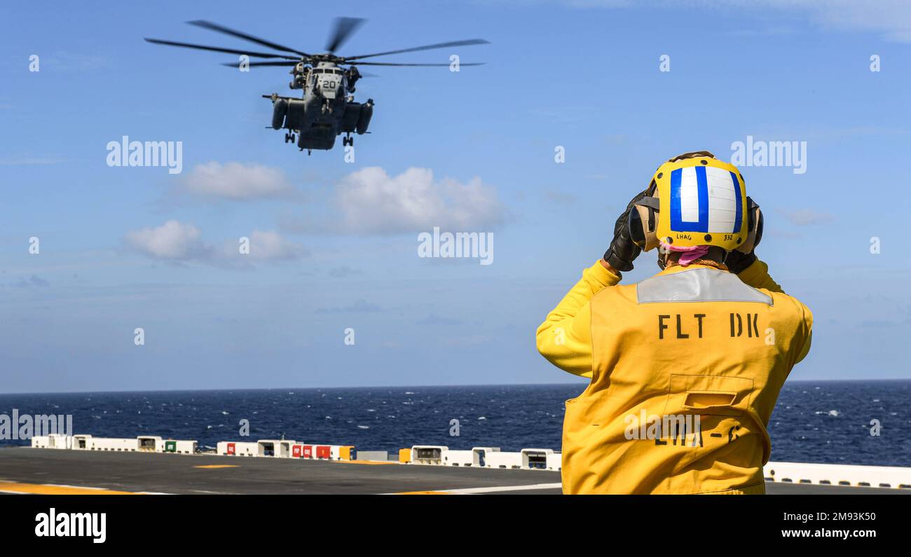 PHILIPPINE SEA (Jan. 13, 2023) Aviation Boatswain’s Mate (Handling) Airman Zachary Phillips, from San Jose, California, assigned to the forward-deployed amphibious assault carrier USS America (LHA 6),directs a CH-53E Super Stallion helicopter from Marine Heavy Helicopter Squadron (HMH) 465 to land on the flight deck while sailing underway in the Philippine Sea, Jan. 13. America, lead ship of the America Amphibious Ready Group, is operating in the 7th Fleet area of operations to enhance interoperability with allies and partners and serve as a ready-response force to defend peace and stability i Stock Photo