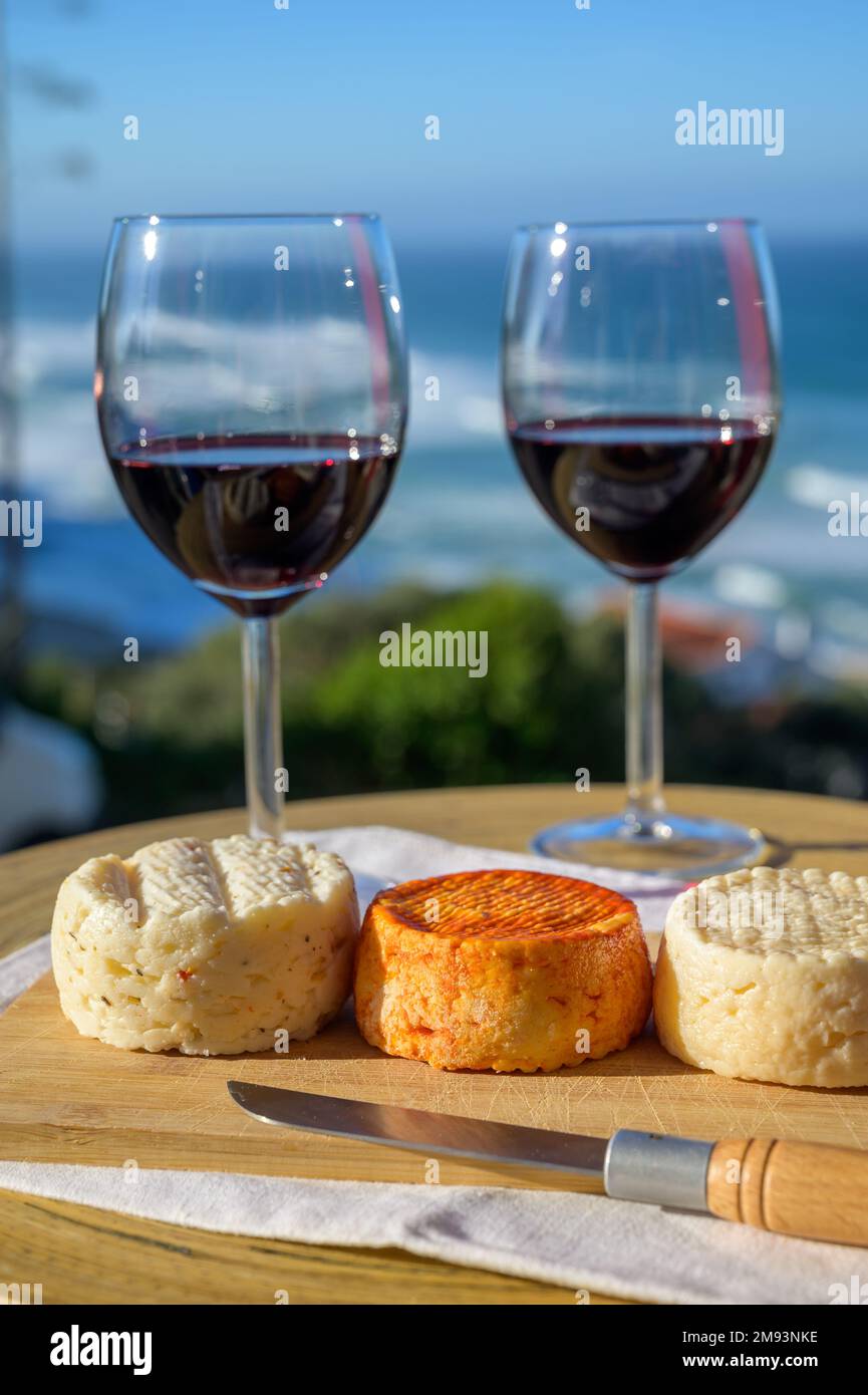 Food and wine pairing, red dry Portuguese wine and variety of goat, sheep, cow cheeses made with paprika, herbs in Portugal served with view on blue A Stock Photo