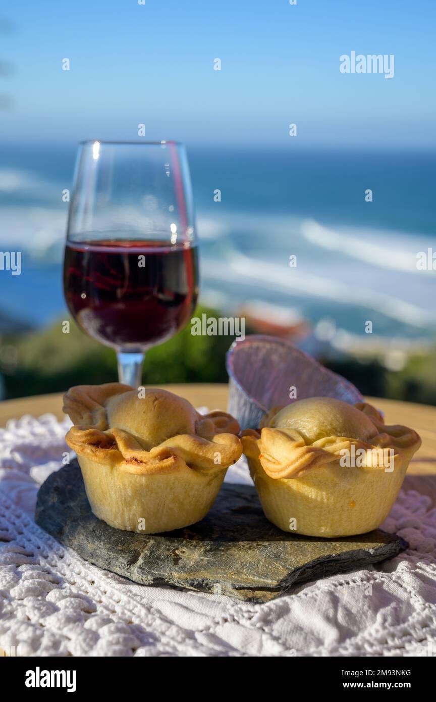 Pairing of Portugeese food and drink, glass of tawny porto wine and chicken  pie empada de frango, served outdoor with view on blue sunny Atlantic ocea  Stock Photo - Alamy