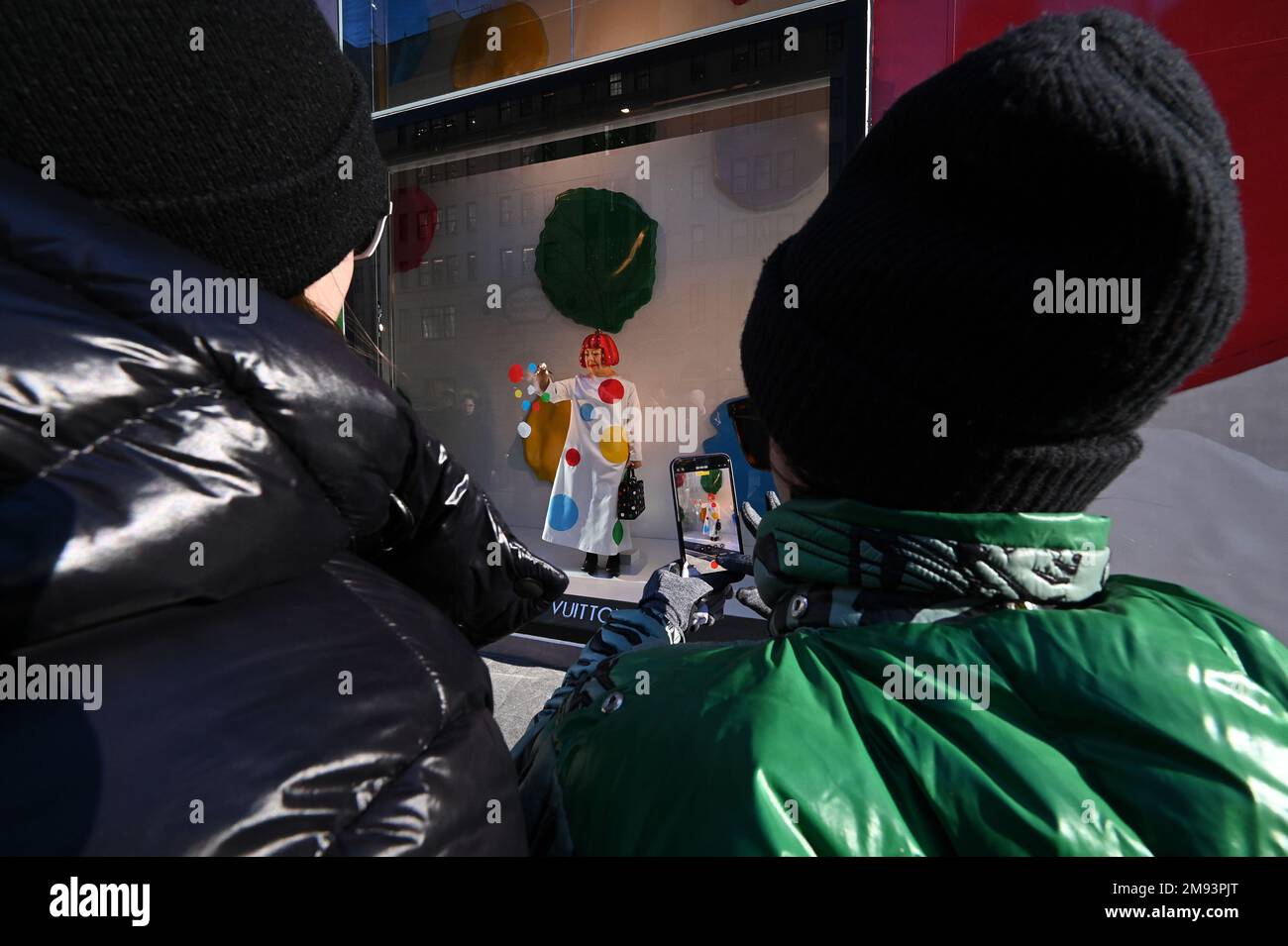 People use their smartphones to take pictures of the Yayoi Kusama robot  painting spots on the window of the luxury retailer Louis Vuitton's Fifth  Avenue store, New York, NY, January 9, 2023.