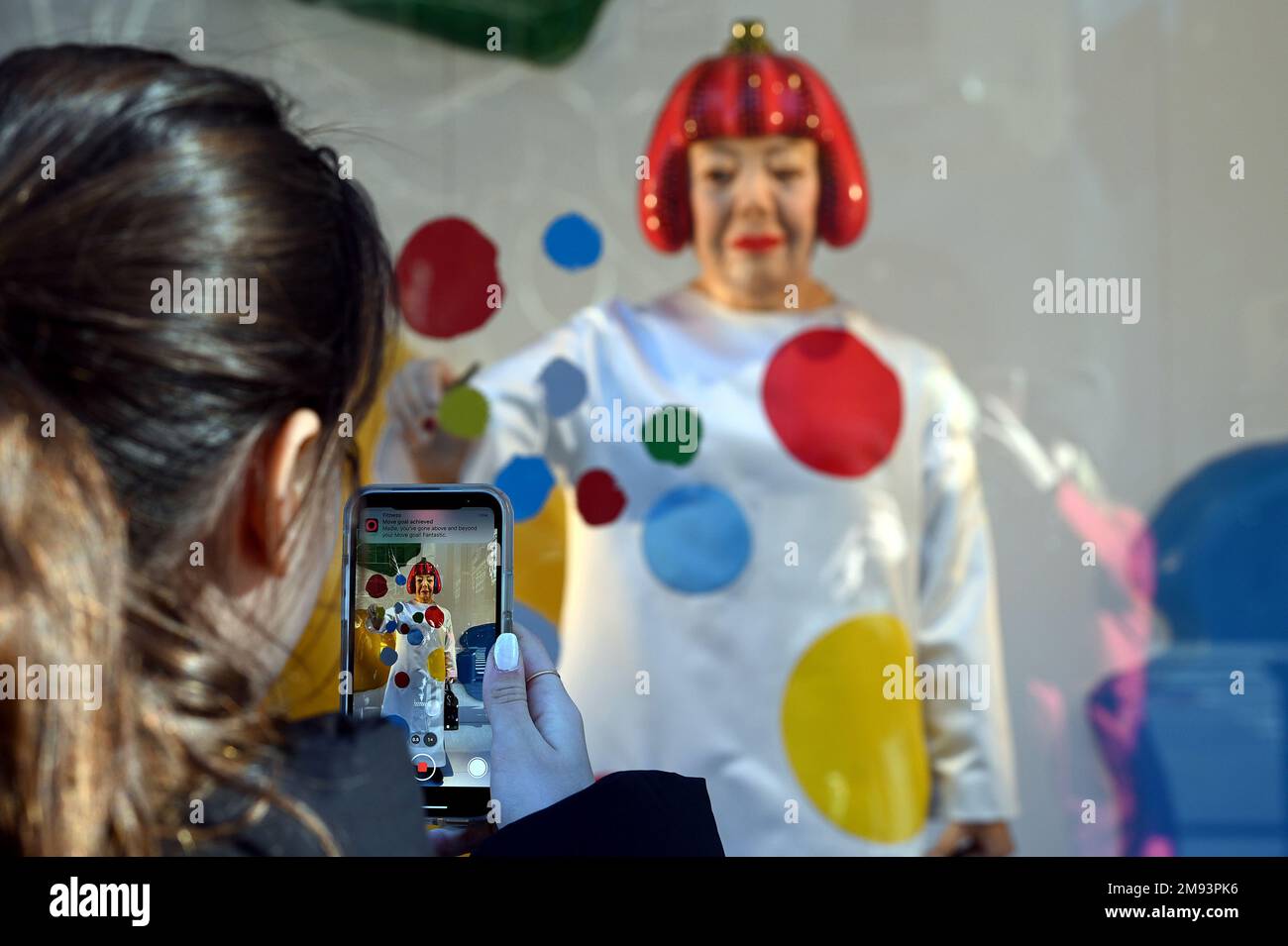 People use their smartphones to take pictures of the Yayoi Kusama robot  painting spots on the window of the luxury retailer Louis Vuitton's Fifth  Avenue store, New York, NY, January 9, 2023.