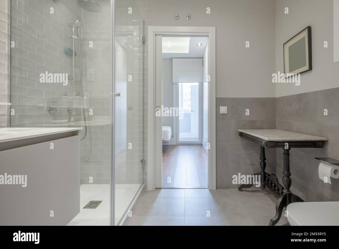 Designer bathroom with marble sink under wall-mounted mirror and shower with tempered glass partitions and access door to an en-suite bedroom Stock Photo