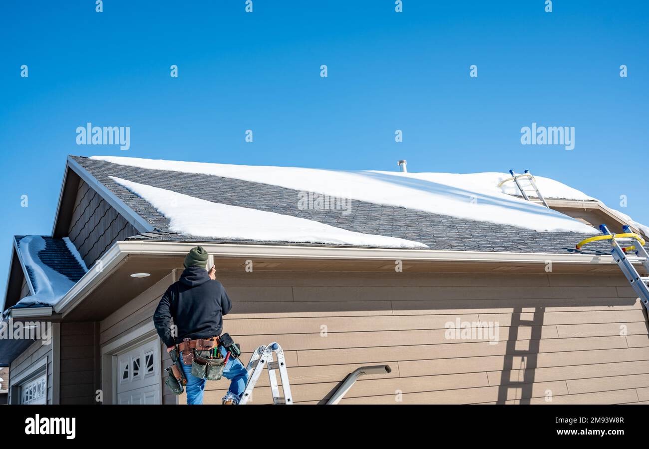 Contractor installing gutters on a residential building in the winter ...