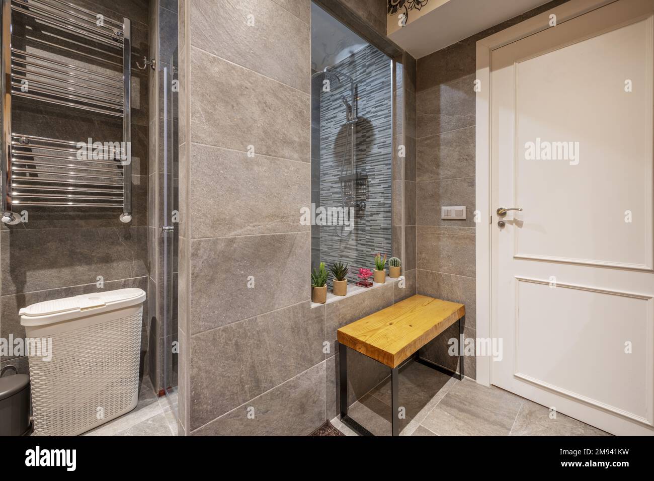 Shower cabin of a bathroom with light slate tiling, wooden plank seat and chrome metal radiator Stock Photo