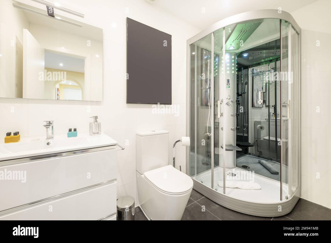 Bathroom with built-in mirror, white chest of drawers with sink and galactic shower cabin with jets, RGB lights, FM radio, seat and mirrors Stock Photo