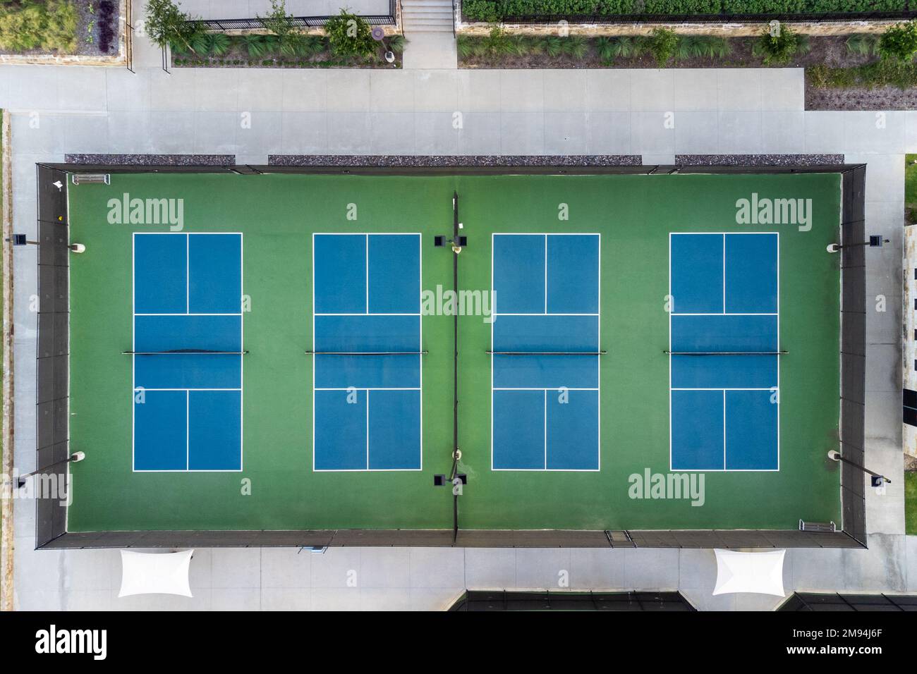 View from above, aerial view of four blue public, empty tennis courts, tennis playgrounds in the summertime outdoor. Stock Photo