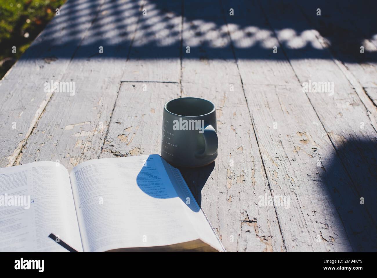 An open book and a mug on an old, rustic-looking porch. - Stock Image