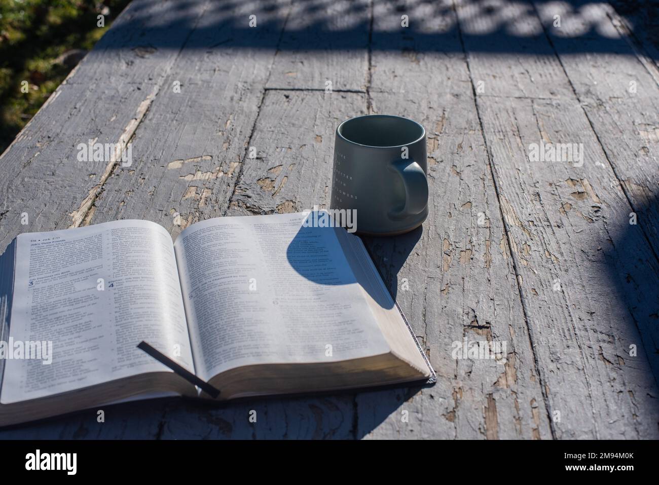 An open book and a mug on an old, rustic-looking porch. - Stock Image