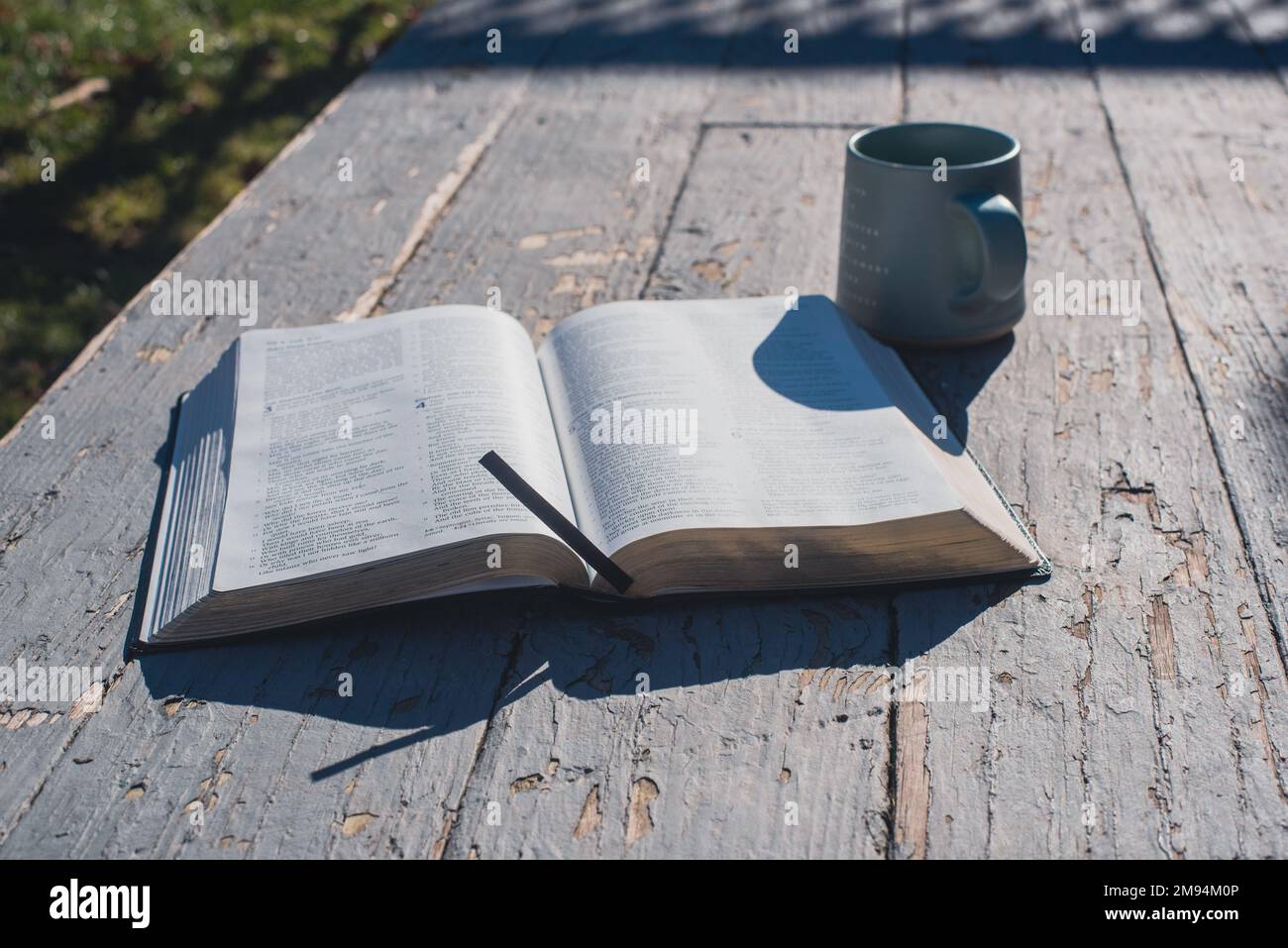 An open book and a mug on an old, rustic-looking porch. - Stock Image