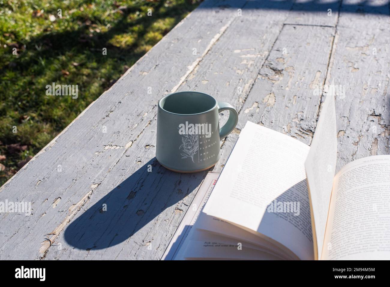 An open book and a mug on an old, rustic-looking porch. - Stock Image