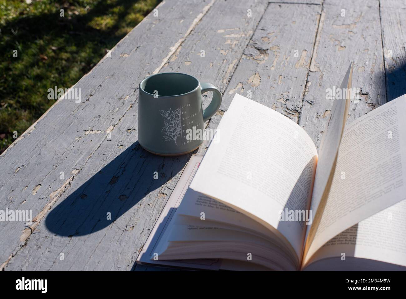 An open book and a mug on an old, rustic-looking porch. - Stock Image