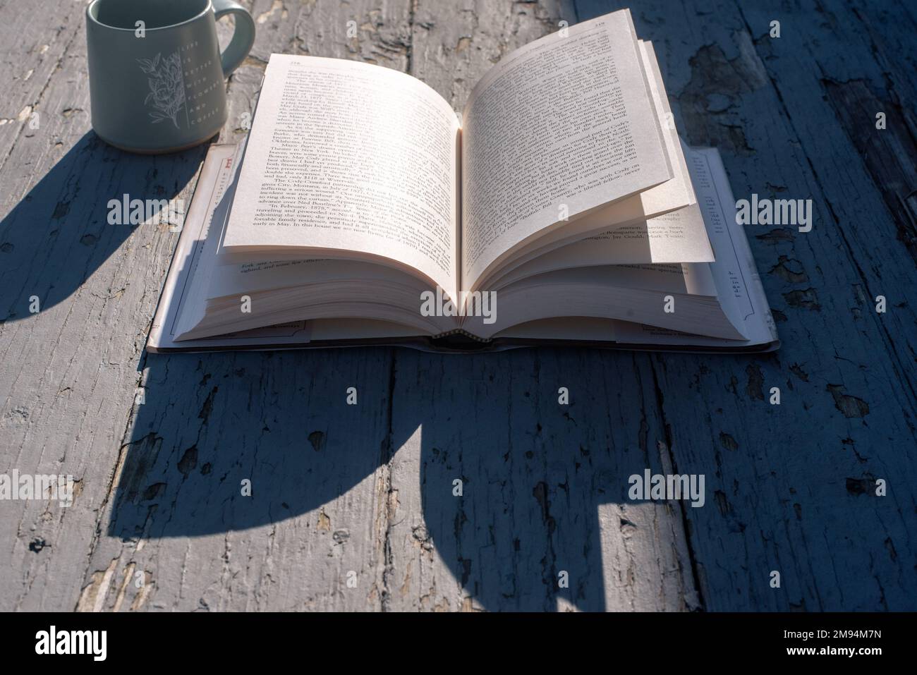 An open book and a mug on an old, rustic-looking porch. - Stock Image