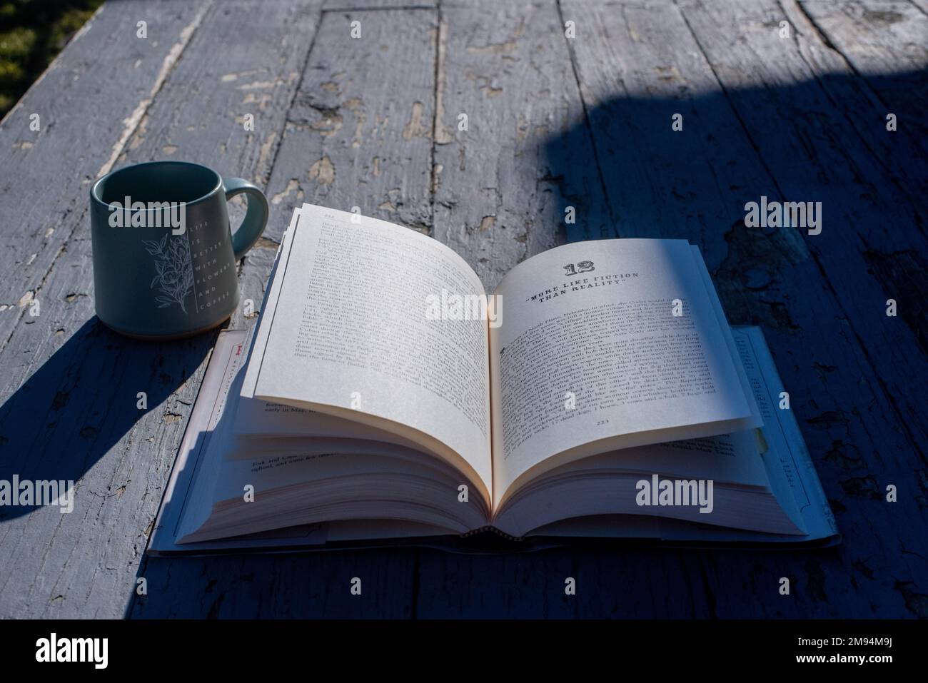 An open book and a mug on an old, rustic-looking porch. - Stock Image