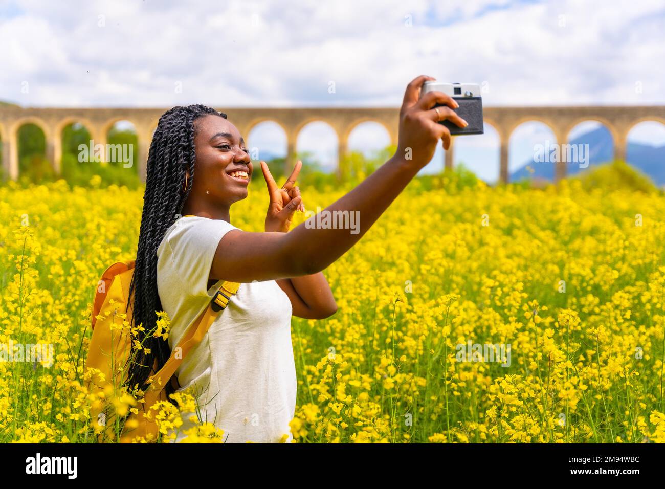 Selfie in nature with a vintage camera, a girl of black ethnicity with braids, a traveler, in a field of yellow flowers Stock Photo