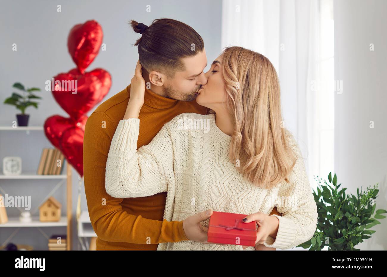 Beautiful, young couple at home in romantic atmosphere congratulate each other on Valentine's Day and give gifts. Stock Photo