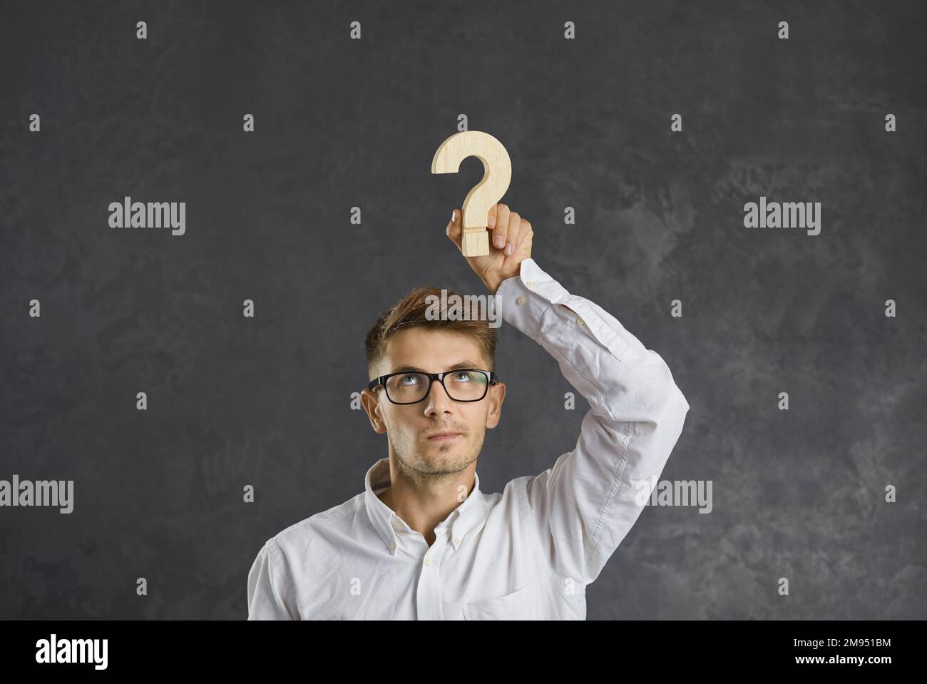 Embarrassed businessman with emotion of doubt on his face holding wooden question mark over his head Stock Photo